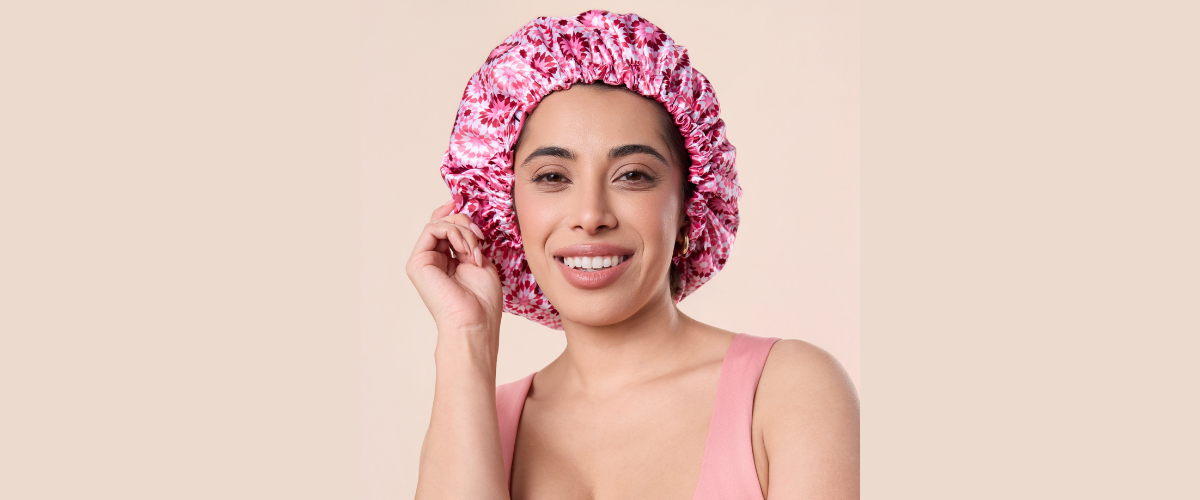 A woman wears a pink Bounce Curl bonnet in front of a tan background
