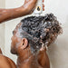 Person in the shower lathers hair while squeezing Bounce Curl shampoo onto scalp.