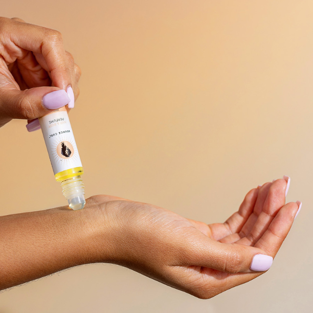 Hand applying Bounce Curl roll-on perfume oil to wrist on a warm beige background